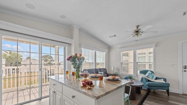 A spacious kitchen with a large island, a dining area with a blue chair, and a view of a residential neighborhood. - Sunny Gulf Coast Getaway-Near Beach-Shared Pool! (Fort Myers Beach)
