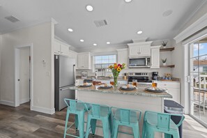 A modern kitchen with white cabinets, a central island with bar stools, a large window, and a view of the outdoors.