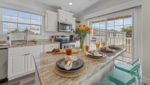 A modern kitchen with white cabinets, a granite countertop, and a large window overlooking a backyard. - Sunny Gulf Coast Getaway-Near Beach-Shared Pool! (Fort Myers Beach)