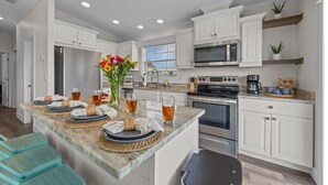 A modern kitchen with white cabinetry, a central island with a vase of flowers, and a breakfast setup. - Sunny Gulf Coast Getaway-Near Beach-Shared Pool! (Fort Myers Beach)