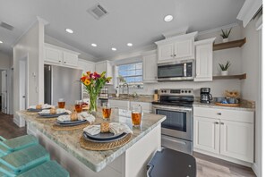 A modern kitchen with white cabinetry, a central island with a vase of flowers, and a breakfast setup.