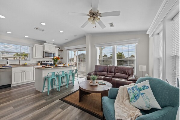A spacious living area with a brown leather sofa, teal chairs, and a coffee table.