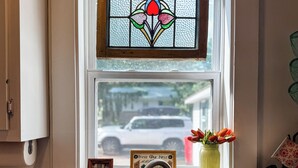 A kitchen with a stainless steel sink, a wooden cutting board, a green dish soap bottle, and a window with a stained glass design.