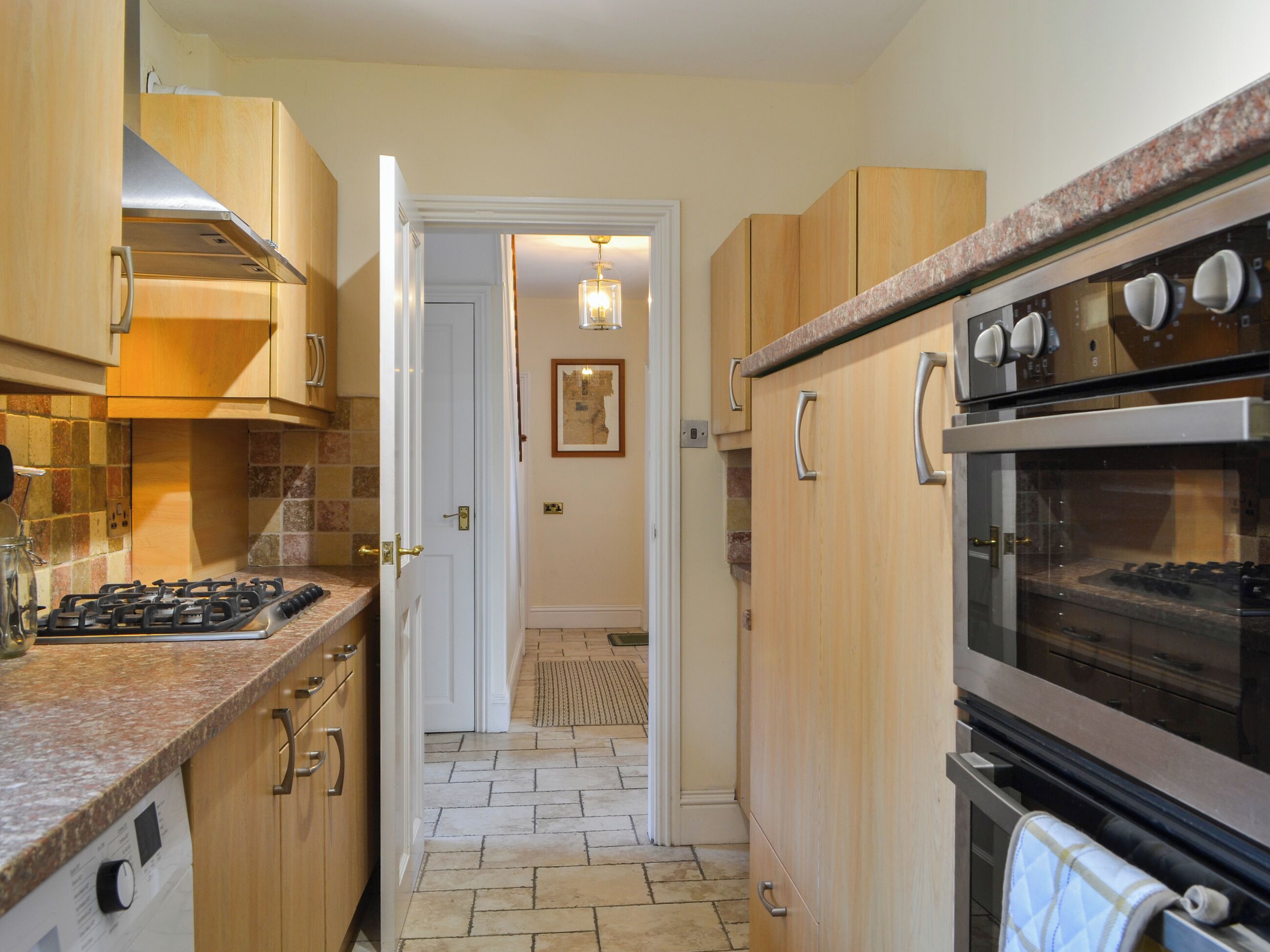 Eine Küche mit Holzausstattung, einem Gasherd, einem Backofen und einer gefliesten Spritzschutzwand.