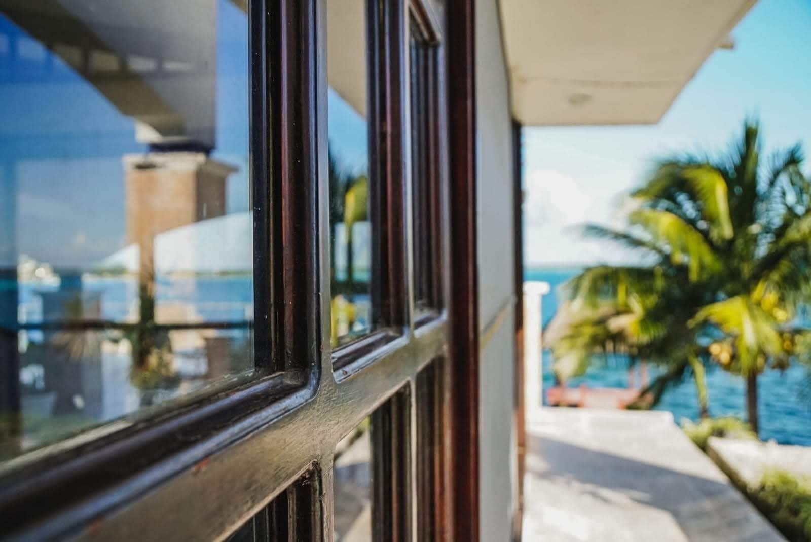 A view from a window of a building with a balcony overlooking a body of water and palm trees.