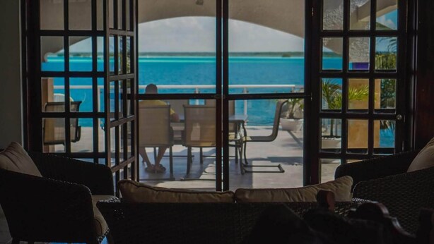A room with a view of a pool and a beach. There are two chairs and a table in the room.