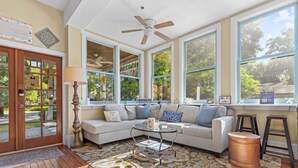 A sunlit living room with a large window, a ceiling fan, and a wooden floor. - GNV Downtown Estate- Sleeps 16 - Groups & Events (Gainesville)