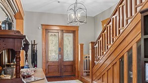 A grand entryway with a wooden staircase, a chandelier, and a large double door with intricate designs. - GNV Downtown Estate- Sleeps 16 - Groups & Events (Gainesville)