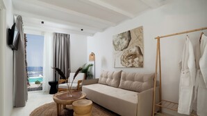 A modern living room with a beige sofa, a round wooden coffee table, and a view of the ocean through large windows.