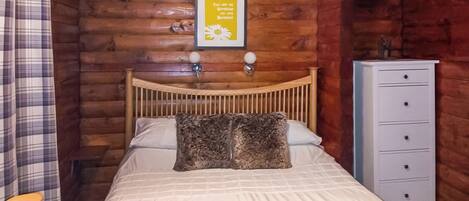 A wooden cabin bedroom with a bed, a dresser, and a framed sign on the wall.