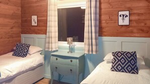 Een kamer met twee bedden, een nachtkastje, een raam met gordijnen en decoratieve muurkunst.