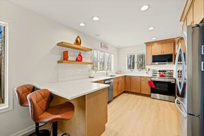 Una cocina moderna con encimeras blancas, armarios de madera, un refrigerador de acero inoxidable y un horno empotrado.