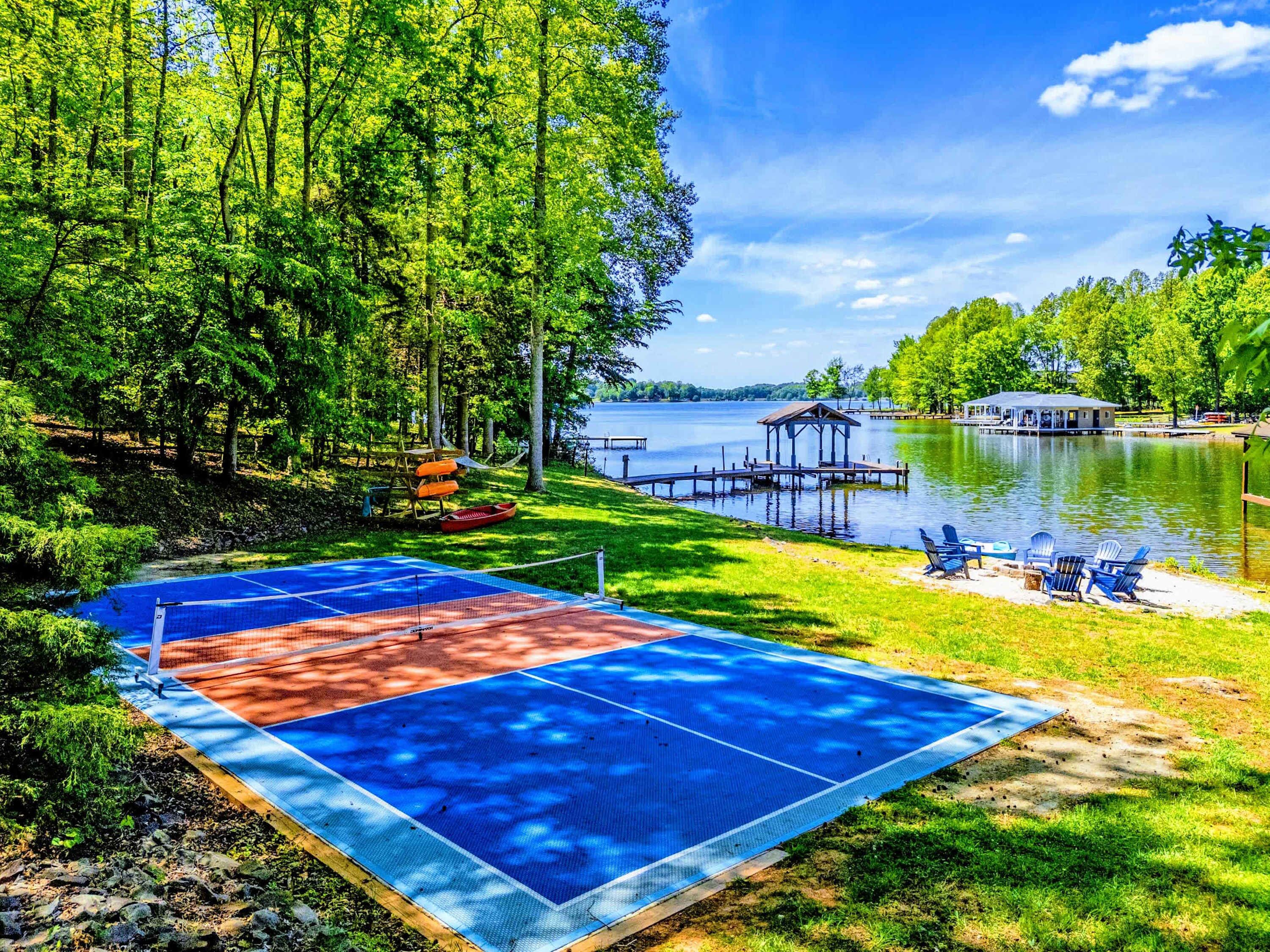 A lakeside tennis court with a dock, chairs, and a small pavilion.