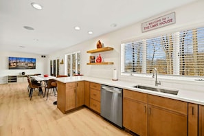 A modern kitchen with wooden cabinets, a dishwasher, and a view of the lake through large windows. - Lakefront Lake Anna with Dock, Hot Tub, Game Room (Bumpass)