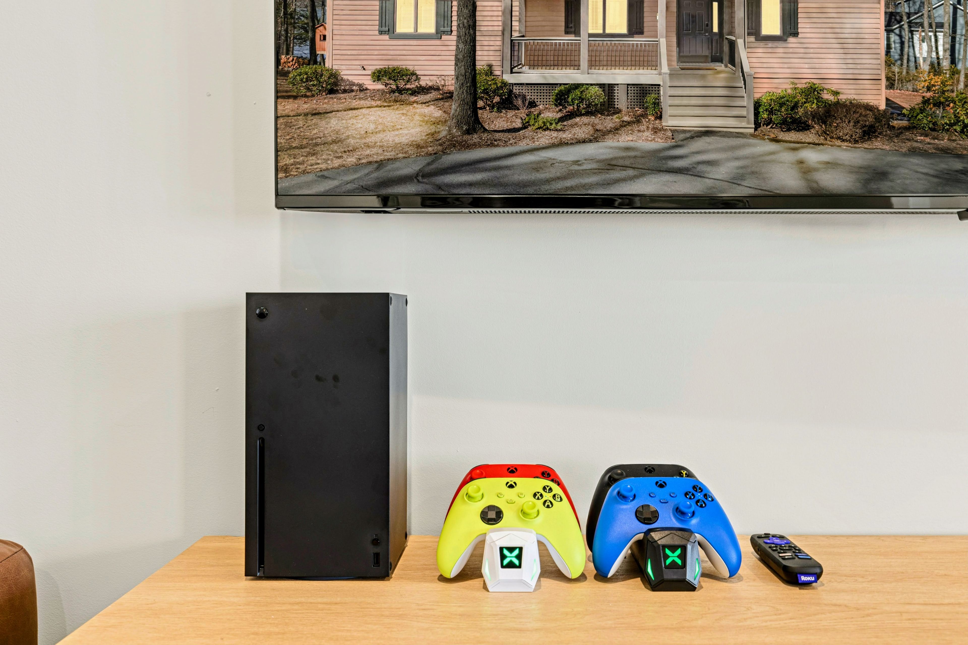 A gaming setup with a black console, two controllers, and a remote on a wooden table.