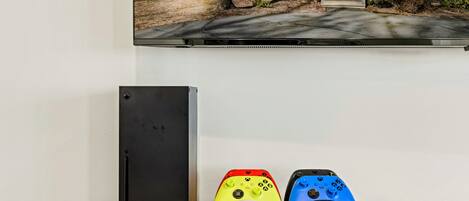A gaming setup with a black console, two controllers, and a remote on a wooden table.