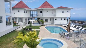 A two-story white building with a red roof, a swimming pool, and outdoor seating. - Lavender Moon Villas (Ocho Rios)