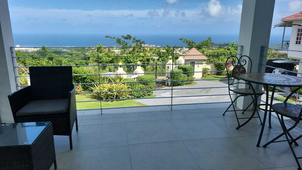 A balcony with a view of the ocean, a dining table, and two chairs. - Lavender Moon Villas (Ocho Rios)
