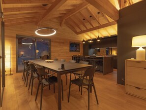 A spacious dining area with a long table and chairs, a kitchen with modern appliances, and a wooden ceiling with exposed beams. - Brand-new, top-of-the-range chalet with panoramic views (sauna, steam room, billiards) (Les Angles)