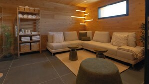 Interior moderno de cabana de tronco, com sofá seccional, pequena mesa redonda e estante de madeira com toalhas.