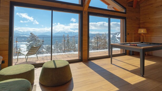 Quarto espaçoso com grandes janelas que oferecem vista para montanhas cobertas de neve e um lago.
