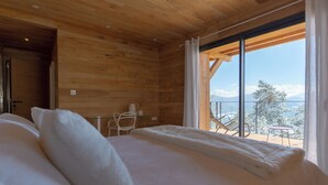 Quarto com uma cama grande, paredes de madeira, porta de vidro que dá para o exterior e vista para árvores cobertas de neve.