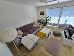 Uma sala de estar moderna com um sofá, uma mesa de centro, um tapete, uma planta e uma escrivaninha com um computador.