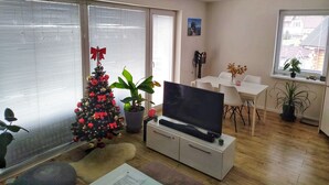 A modern living room with a flat-screen TV on a cabinet, a Christmas tree, and a dining area with a table and chairs.