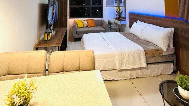 A modern hotel room with a sofa, a bed, a TV, and a dining table. - Sassy and Classy Fully Furnished Studio Unit located Cebu City Centre (Cebu City)