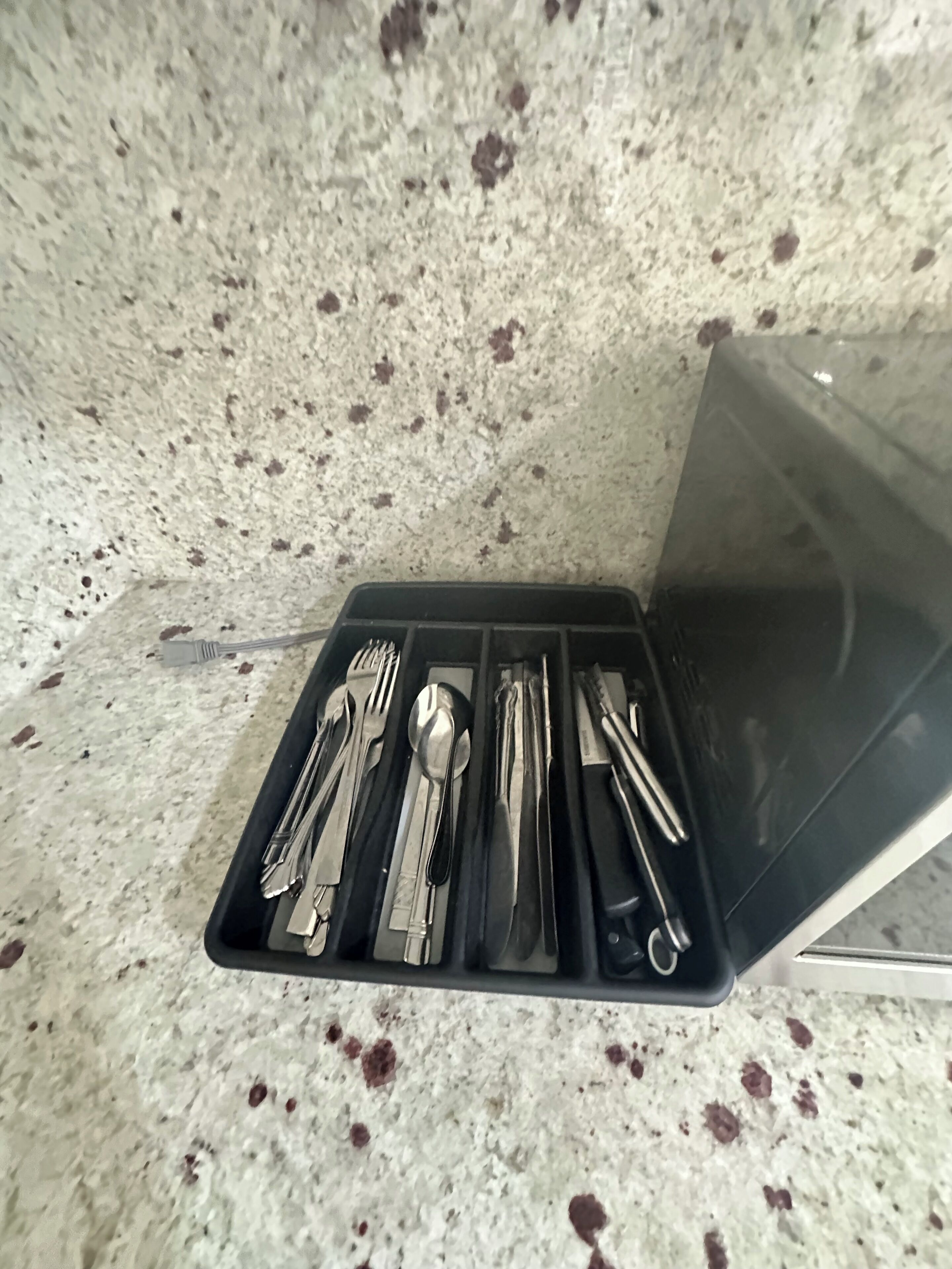 Un juego de cubiertos ordenado en una bandeja negra sobre una encimera de granito moteado.