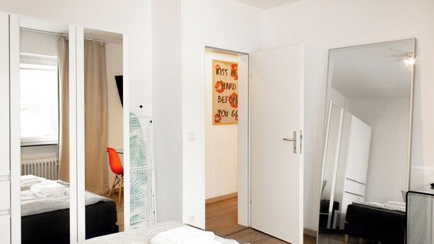Een slaapkamer met een bed, een spiegel en een deur naar een andere kamer.