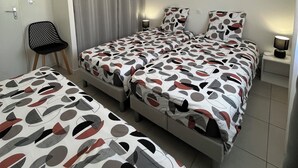 Moderni makuuhuone, jossa on parivuode, tuoli, yöpöytä ja seinään kiinnitetty valaisin.