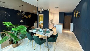 A modern dining area with a marble table, green upholstered chairs, and a large potted plant.