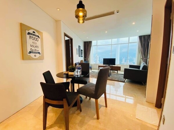 Una habitación de hotel moderna con zona de comedor, sofá y un amplio ventanal con vistas a la ciudad.