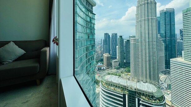 A room with a large window overlooking a cityscape, featuring modern buildings and a prominent skyscraper.