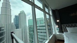 A hotel room with a large window offering a view of the Petronas Towers and other buildings.