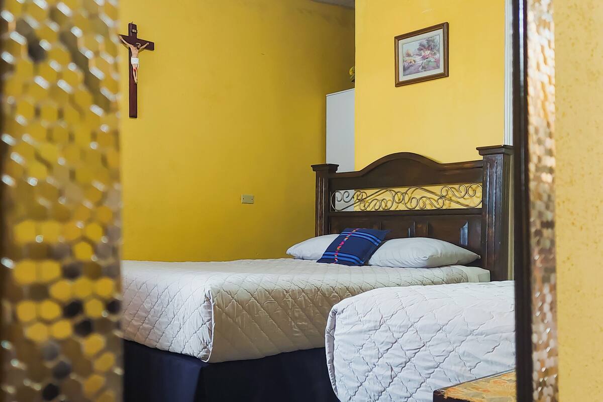 Una habitación con dos camas, cabecera de madera, una cruz en la pared y un cuadro enmarcado.