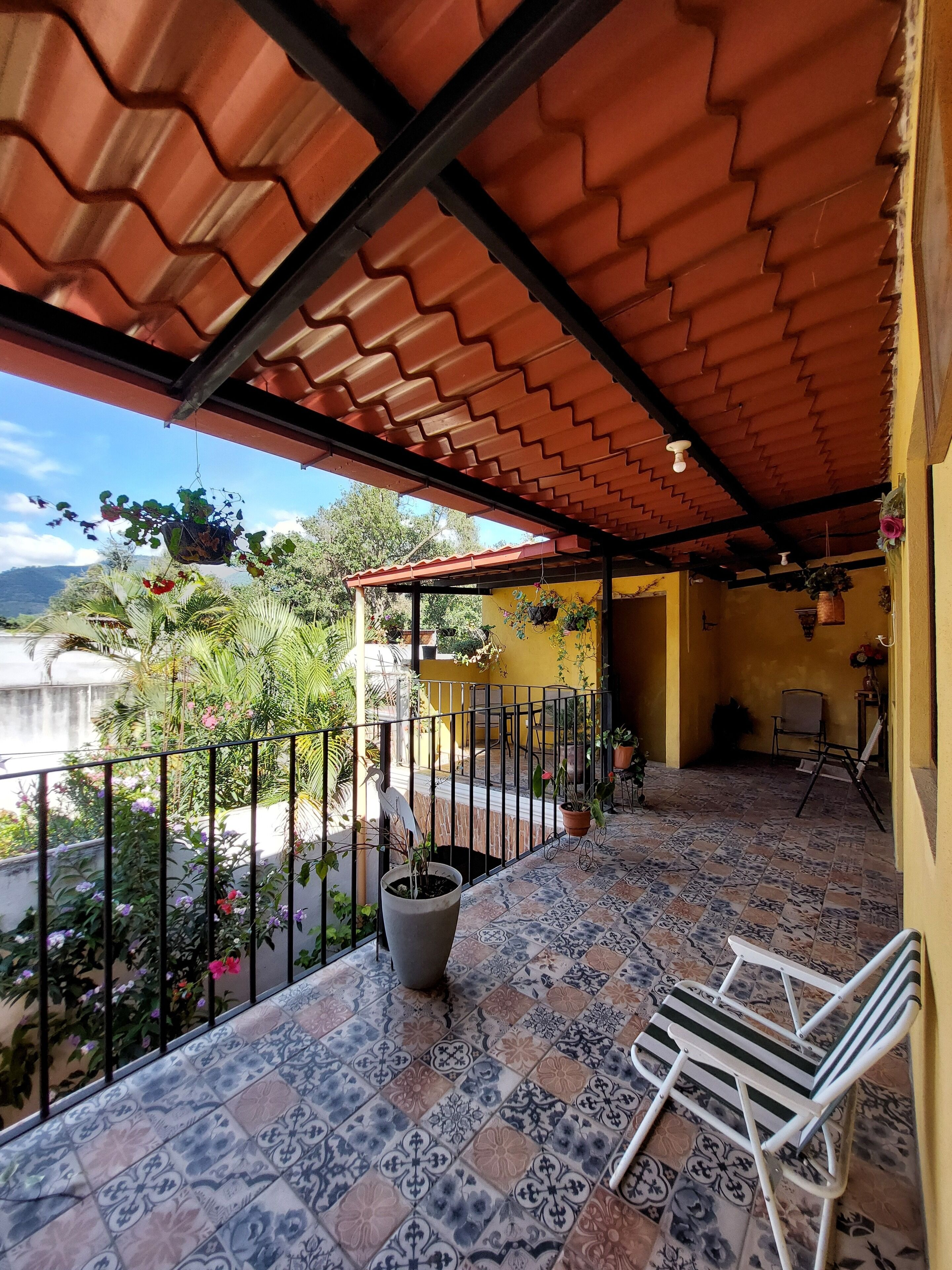 Une terrasse couverte avec un sol carrelé, une rambarde en métal et un fauteuil suspendu.