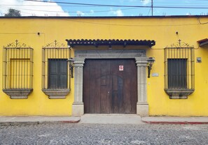 A yellow building with a wooden door and two windows with metal bars. - Hotel Nolasco (Antigua Guatemala)
