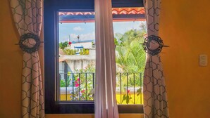 A window with patterned curtains, a view of a building with a red roof, and greenery outside. - Hotel Nolasco (Antigua Guatemala)