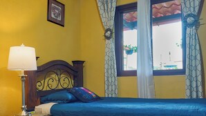 A room with two beds, a nightstand, a lamp, a framed picture on the wall, and a window with curtains. - Hotel Nolasco (Antigua Guatemala)
