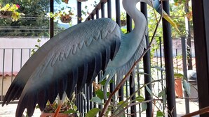 A large bird sculpture on a metal railing, surrounded by greenery and hanging plants. - Hotel Nolasco (Antigua Guatemala)
