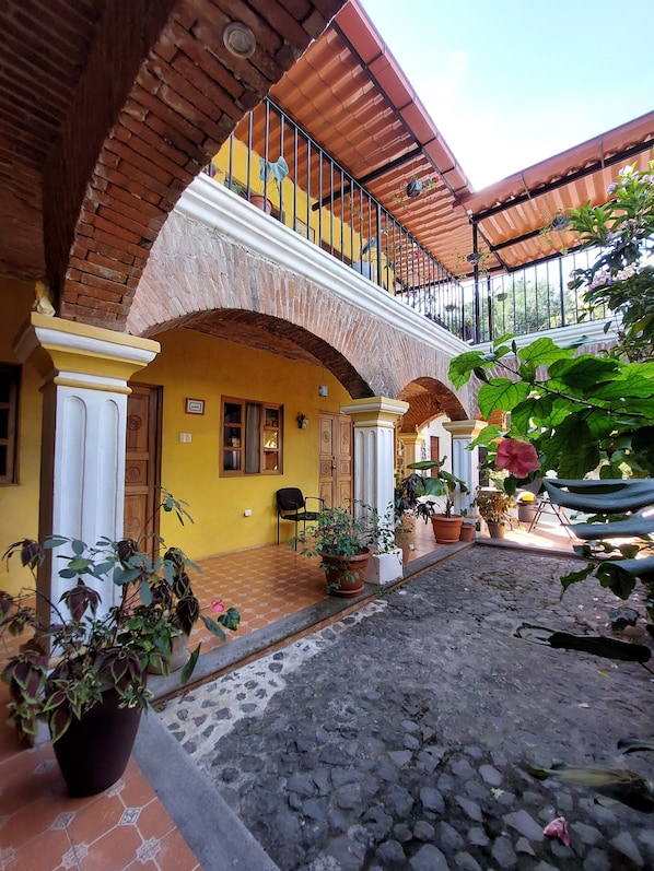 A courtyard with a yellow building, a balcony with metal railings, and potted plants.