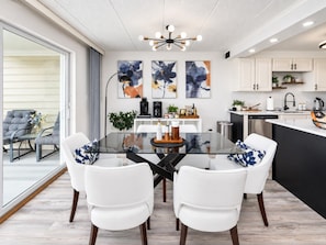 A modern kitchen with white cabinets, a black countertop, and a dining area with a glass table and white chairs. - Bayfront 2BR by Convention Center + Sunsets (Ocean City)