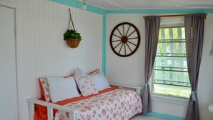 Un dormitorio con cama, ventana con cortinas, un carrusel montado en la pared y una planta colgante.