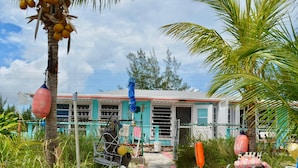 Una casa de color azul, con un porche y una silla, y una palmera.