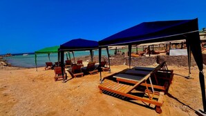 Een strand met ligbedden en parasols, een houten terras, en uitzicht op de zee.