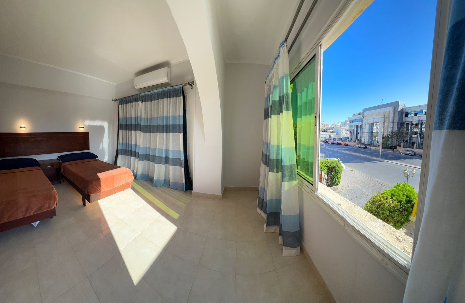 Hotelkamer met twee bedden, een groot raam met gordijnen, uitzicht op de straat en een airconditioning.
