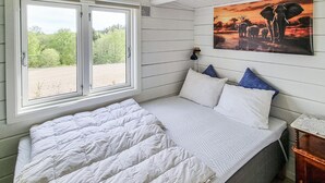 Een slaapkamer met een bed, een raam met uitzicht op groen, een wandlamp en een schilderij van olifanten.