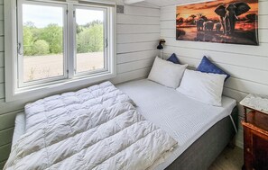 Ein Schlafzimmer mit einem Bett, einem Fenster mit Blick auf Grünflächen, einer Wandlampe und einem Elefantenbild.